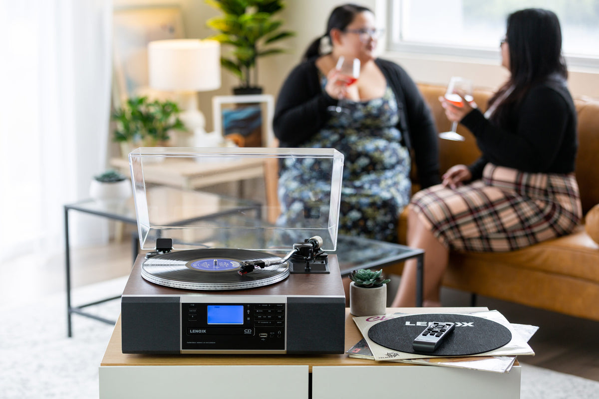 BCD120 Vinyl Turntable in a living room. Two young women visible in the background are sitting on a sofa, drinking wine and chatting while listening to a vinyl record with classical music.
