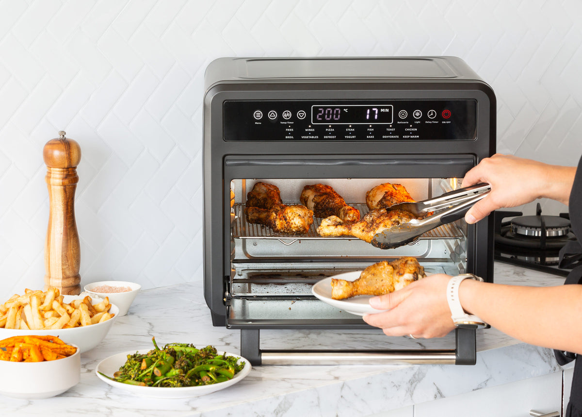 Woman takes perfectly cooked chicken drumsticks out of the air fryer oven.