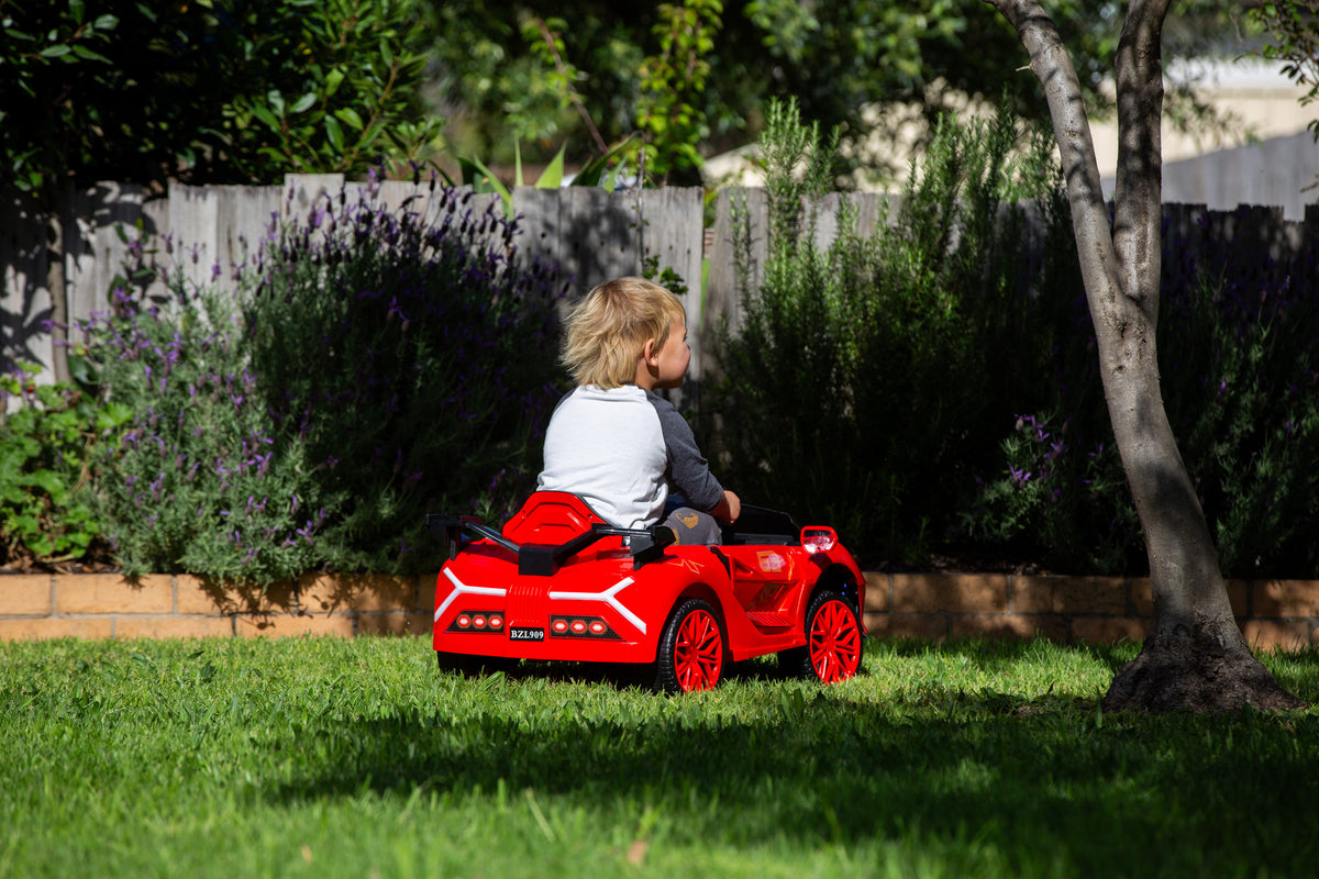 Little boy driving the BZL909 red electric car ride on around a lush backyard.