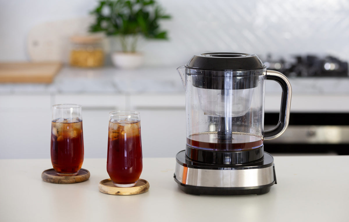 Digital cold brew maker next to 2 tall glasses filled with cold brew coffee in a modern kitchen.