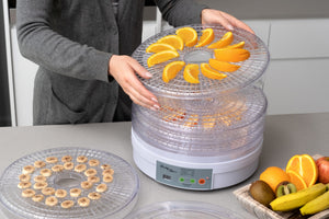 Woman placing a layer of oranges and bananas on the food dehydrator.