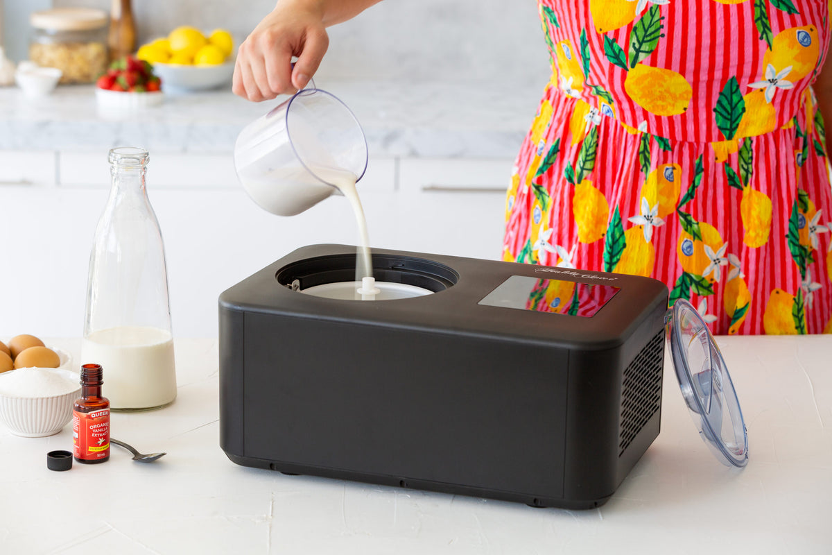 Person pouring liquid into a black ice cream maker on a kitchen counter.