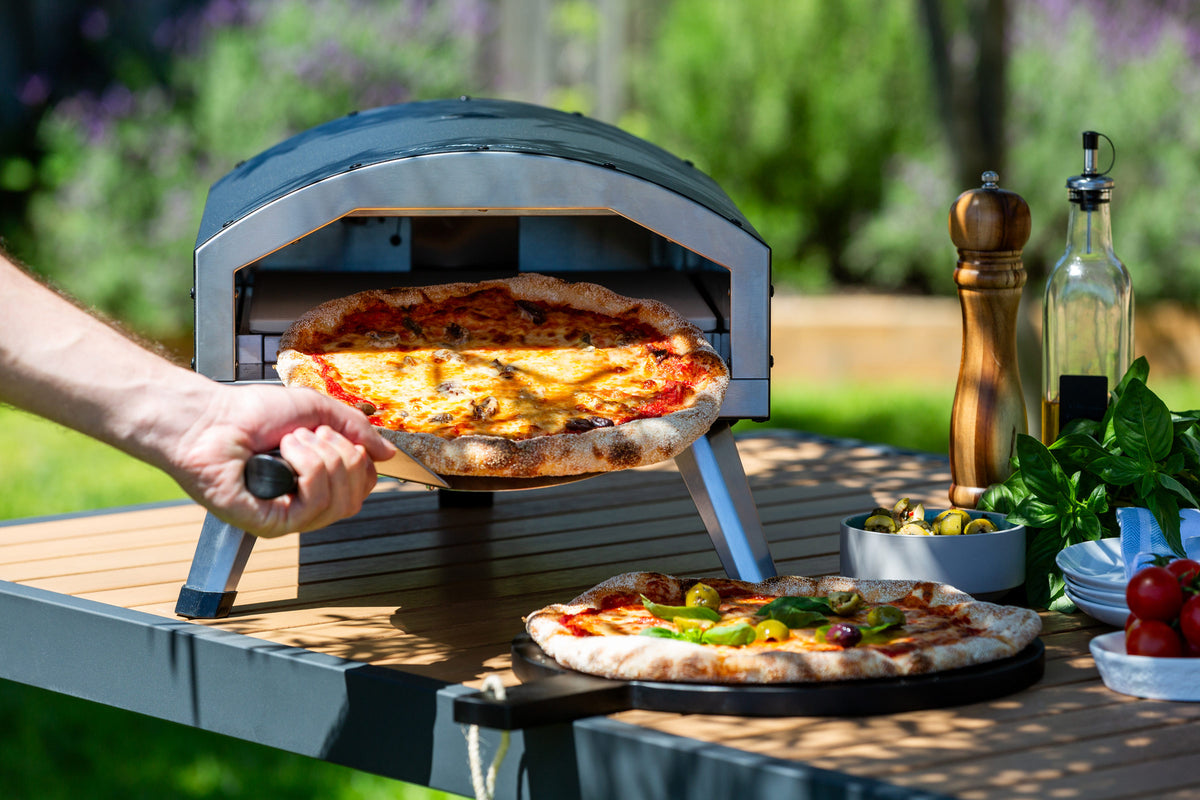 Freshly baked pizza being taken out of the 12" Outdoor Electric Pizza Oven