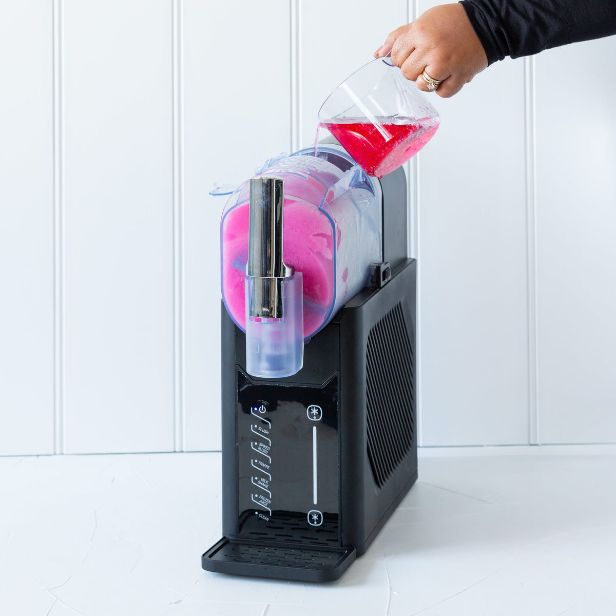 Person pouring pink drink into a black slushie machine against a white background