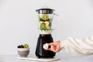 Woman turning on the black table blender filled with kiwi, blackberries and bananas.