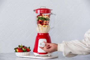 Woman turning on the red table blender filled with strawberries and bananas.