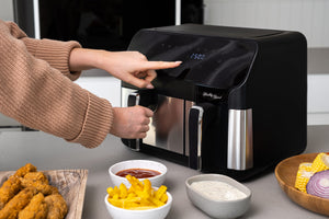Healthy Choice AFDZ100 Digital Dual Zone Air Fryer on a kitchen island with woman's hands on the basket handle and the digital screen.
