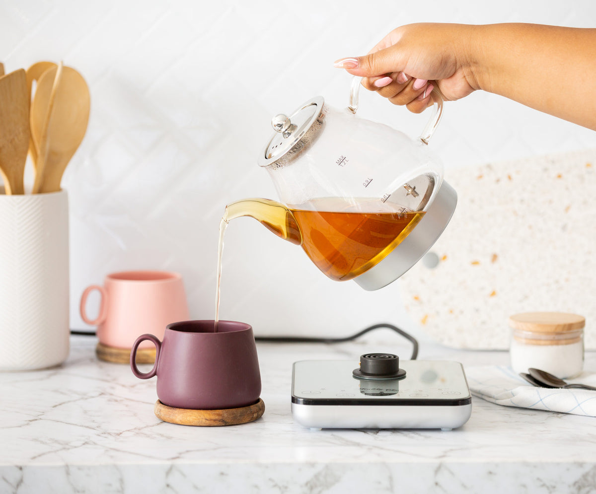 Tea being poured to a purple mug from the glass gooseneck kettle SK200 in a bright kitchen setup.